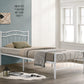 White metal bed frame with bedding in a room with large windows and a lamp.