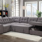 Gray sectional sofa in a living room with a bookshelf and large windows.